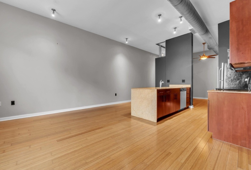 Open-concept living area with light wood-finish flooring, recessed lighting, and a modern kitchen island featuring a sink, integrated dishwasher, and light-toned countertop