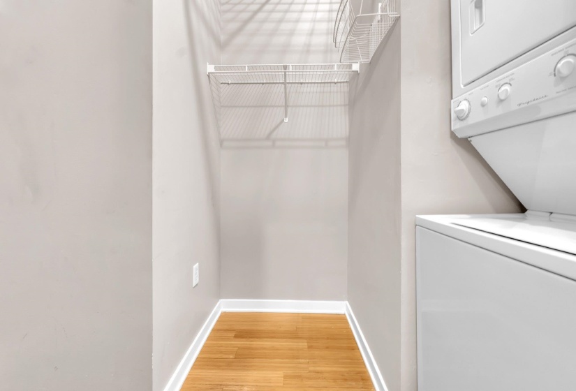 Utility closet featuring stackable laundry appliances, wood-finish flooring, and wire shelving