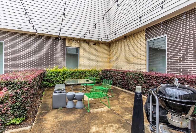 Private concrete patio area featuring string lighting, brick and siding exterior walls, and surrounding shrubbery