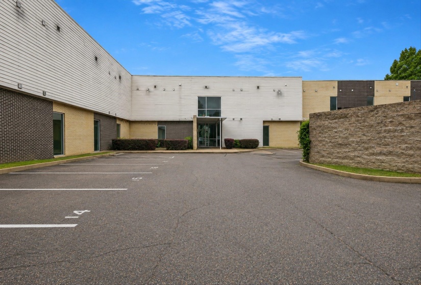 Expansive asphalt parking lot with clearly marked spaces, providing direct access to the building entrance