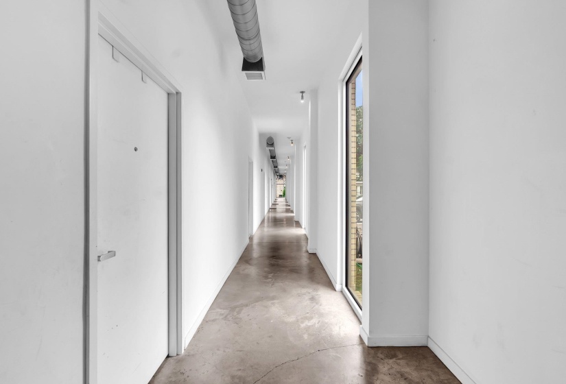 Long hallway featuring concrete flooring and white walls