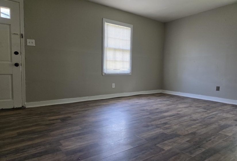 Spacious room featuring wood-finish flooring, neutral gray walls, white baseboards, and a window with blinds