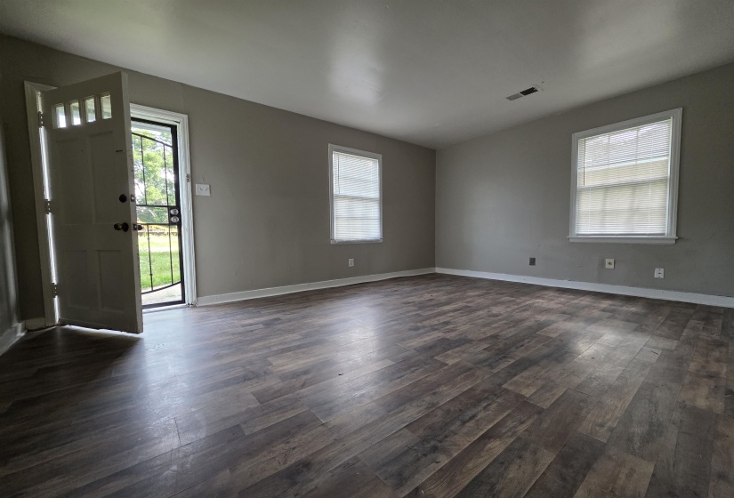 Interior space featuring wood-finish flooring, two windows with blinds, light gray walls, and a front entry door with a security screen