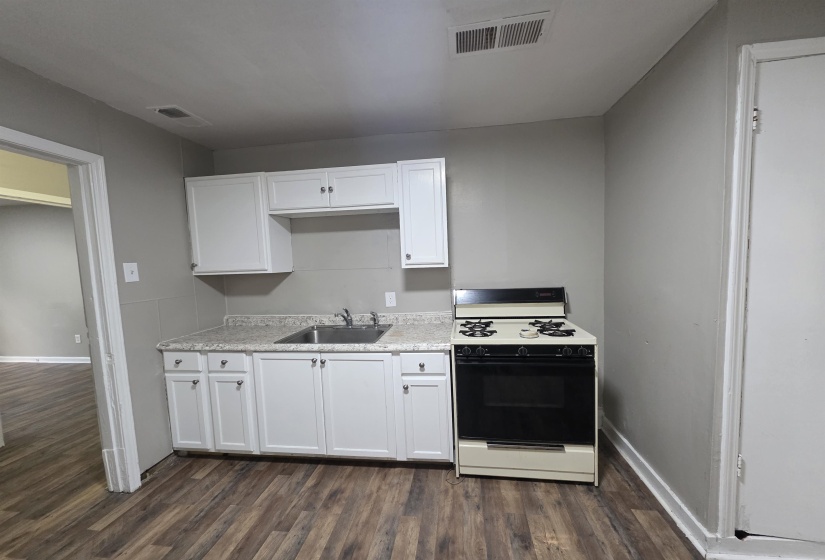 Compact kitchen featuring wood-finish flooring, white cabinetry, a stainless steel sink, light-toned countertops, and a freestanding range