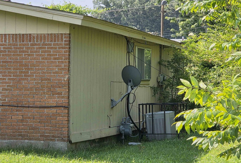 Exterior featuring brick and vertical panel siding, a single-pane window, and an HVAC unit with a protective enclosure