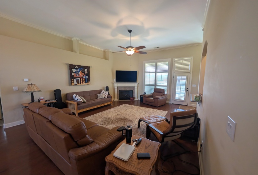 Spacious living area featuring wood-finish flooring, a fireplace with a white mantel, and crown molding