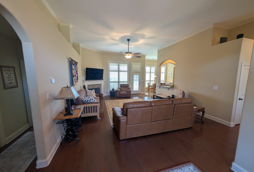 Spacious living area featuring dark wood-finish flooring, a ceiling fan, crown molding, and an arched entryway
