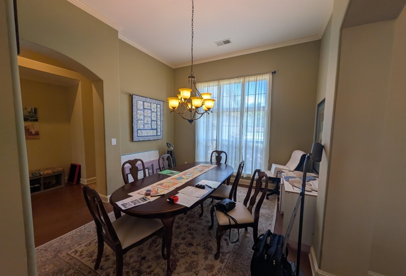 Dining area featuring crown molding, a multi-light chandelier, a large window with sheers, and an arched entryway