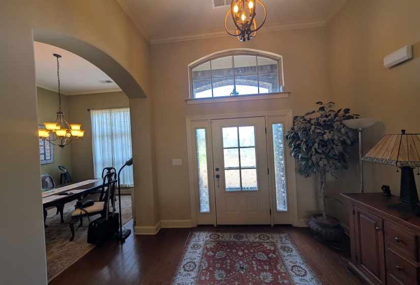 Double-height entry featuring wood-finish flooring, an arched transom window, and a chandelier with decorative scrollwork