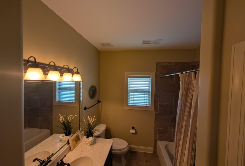 Bathroom featuring a dual-sink vanity with a light-toned countertop, a large mirror, and a four-light fixture