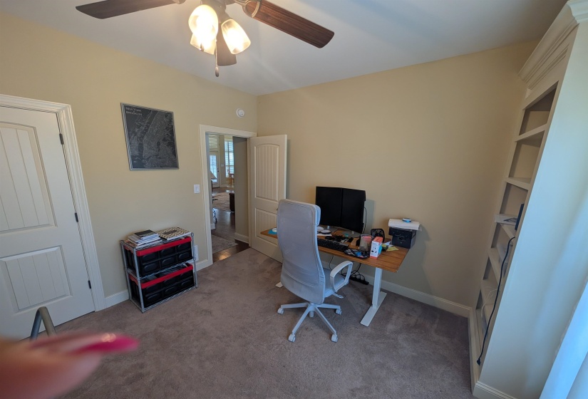 Neutral-toned room featuring a built-in shelving unit, a ceiling fan with integrated lighting, and light-colored carpeting