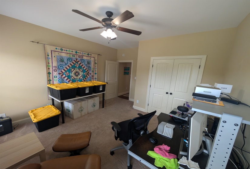 Carpeted room with a ceiling fan, featuring a light beige wall color and white paneled bi-fold closet doors with black hardware