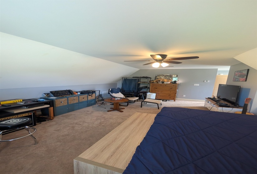 Carpeted room featuring a sloped ceiling, ceiling fan with integrated lighting, and painted walls