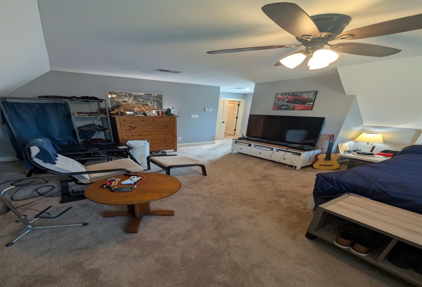 Spacious carpeted room featuring a ceiling fan with integrated lighting, sloped ceiling details, and neutral wall paint