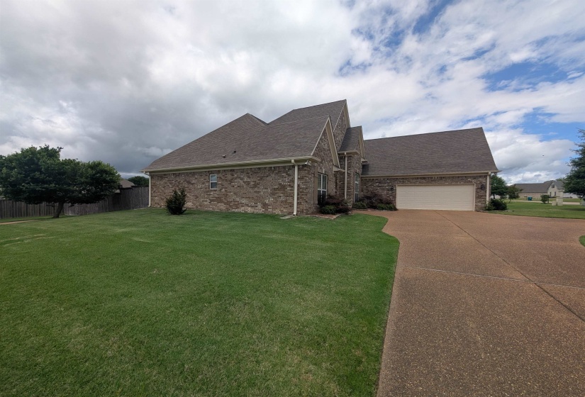 Brick exterior with an attached garage, featuring a gabled roofline, a textured concrete driveway, and a manicured lawn