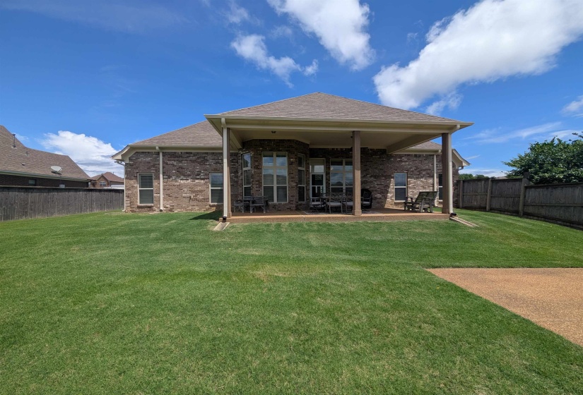 Rear brick exterior featuring a covered patio, multiple windows, and a fenced yard with established lawn