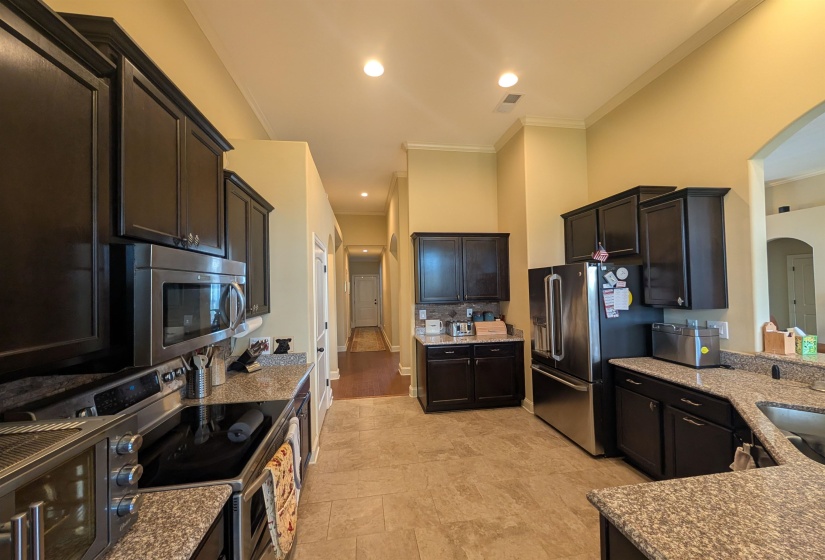 Galley kitchen featuring dark wood cabinetry, stainless steel appliances, granite countertops, and tile flooring