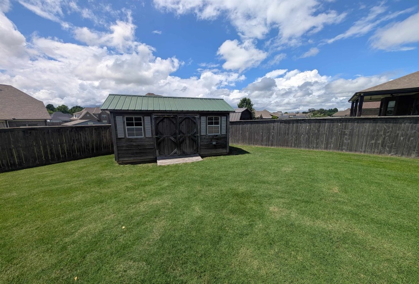 Expansive backyard featuring a lush lawn, privacy fencing, and a storage shed with a green metal roof, double doors, and window accents