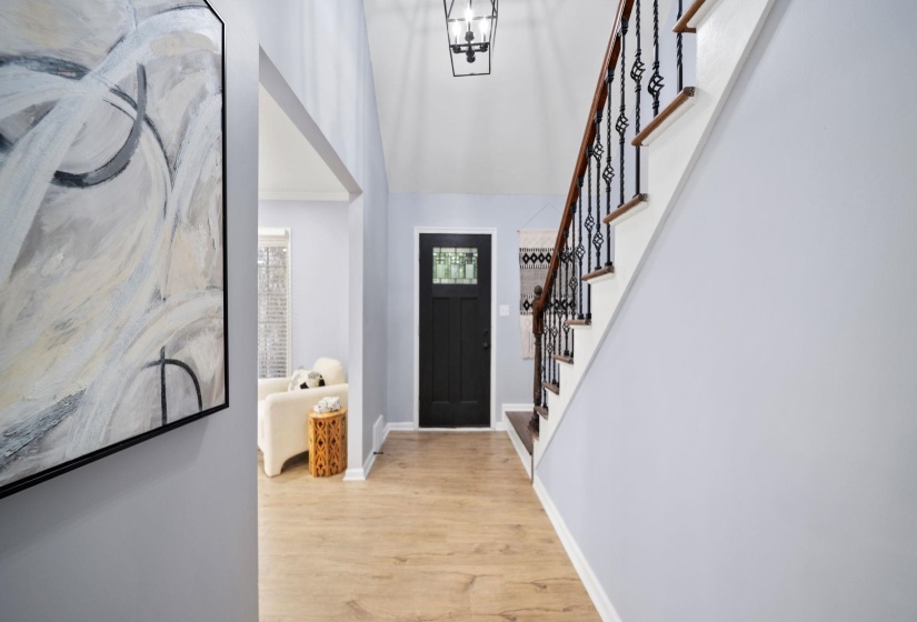 Entryway featuring wood-finish flooring, a dark-paneled door with decorative glass, and a staircase with dark wood handrails and wrought iron balusters