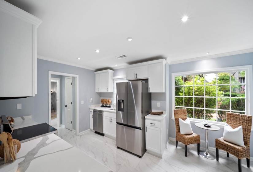 Bright kitchen featuring white cabinetry with brushed nickel hardware, stainless steel appliances, large paneled window, recessed lighting, and light-toned flooring