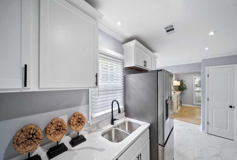Contemporary kitchen featuring white cabinetry with black hardware, a stainless steel refrigerator, white quartz-finish countertops, a dual basin stainless steel sink, and white tile flooring