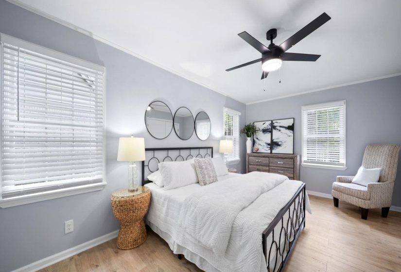 Spacious bedroom featuring light wood-finish flooring, multiple windows with blinds, a ceiling fan with integrated lighting, and crown molding
