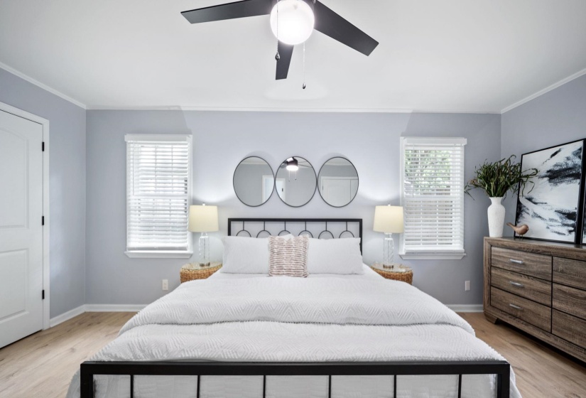 Bedroom featuring wood-finish flooring, two windows with blinds, a white door, a ceiling fan, and decorative wall mirrors