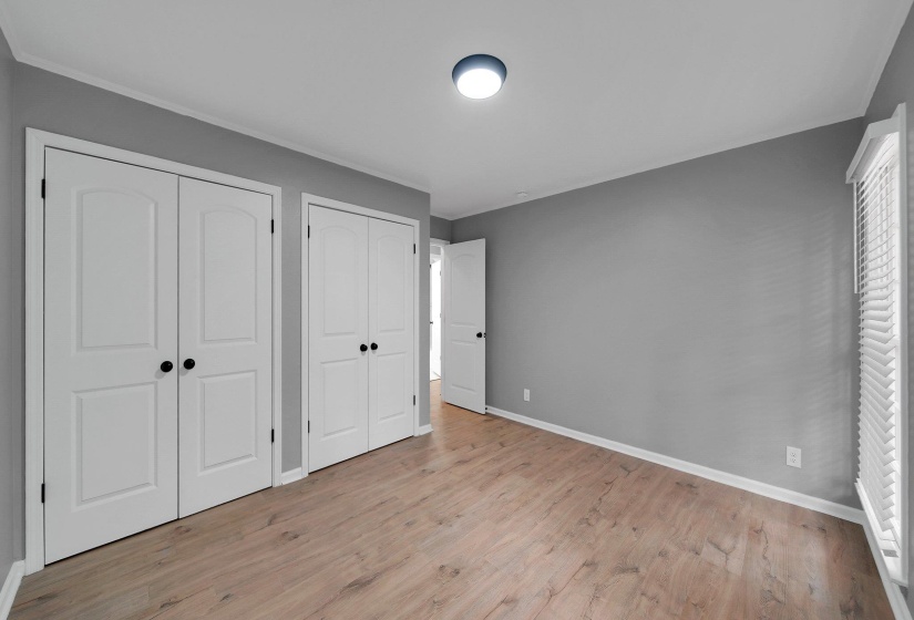 Unfurnished bedroom with multiple closets, light wood-style floors, and crown molding
