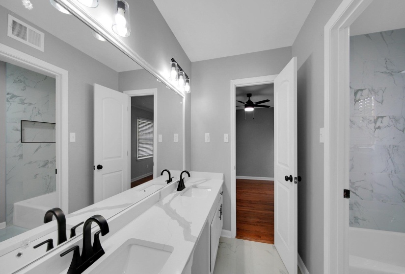 Bathroom with marble finish floors, ceiling fan, double vanity, and a bathtub