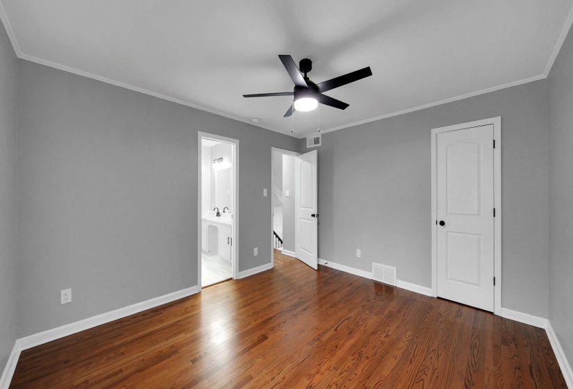 Unfurnished bedroom featuring wood finished floors, crown molding, ensuite bathroom, and a ceiling fan