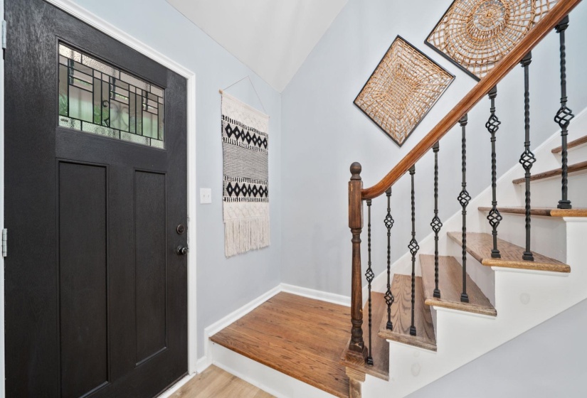 Entryway featuring a black door with leaded glass, wood-finish flooring, and a staircase with decorative wrought iron spindles and a wood handrail