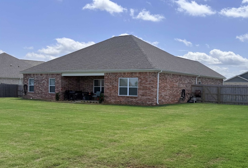 Expansive green lawn surrounds a brick exterior home featuring a covered patio, white-framed windows, and a privacy fence