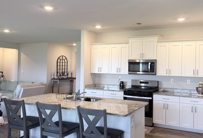 Kitchen featuring an island with a built-in sink and countertop seating, white shaker-style cabinetry, stainless steel appliances, recessed lighting, and wood-finish flooring