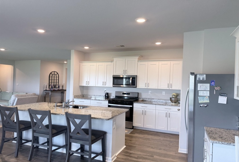 Kitchen featuring an island with a built-in sink, white cabinetry, stainless steel appliances, granite countertops, and wood-finish flooring
