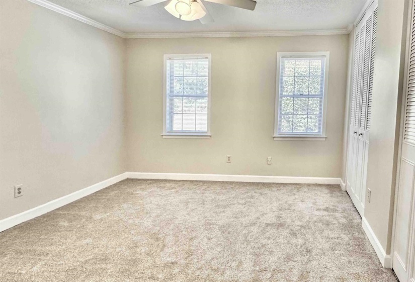 Unfurnished bedroom featuring a textured ceiling, ornamental molding, light carpet, multiple closets, and a ceiling fan