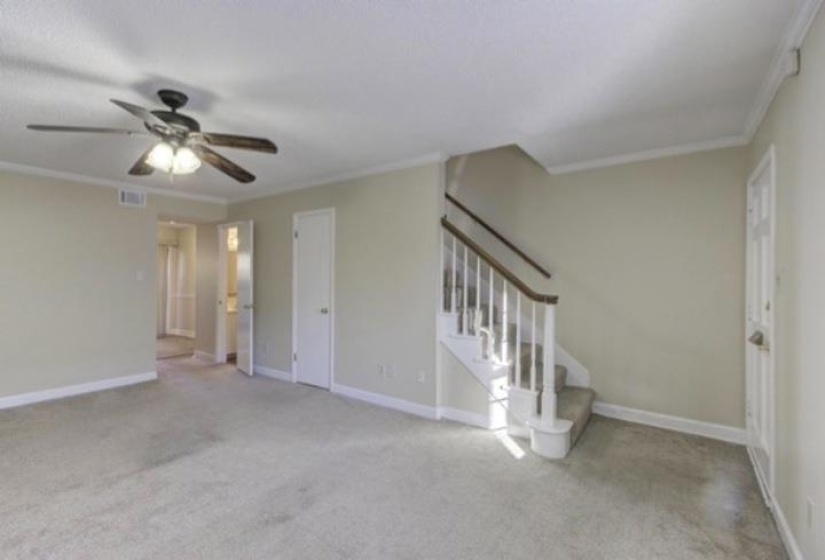 Unfurnished living room featuring stairway, ornamental molding, light carpet, and ceiling fan