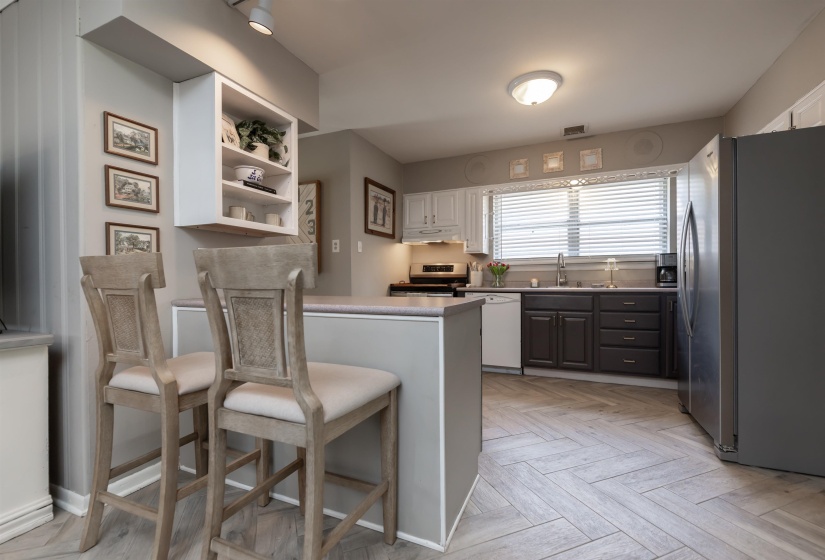 Kitchen featuring an integrated breakfast bar, two-tone cabinetry, stainless steel appliances, a double basin sink, and herringbone pattern wood-finish flooring
