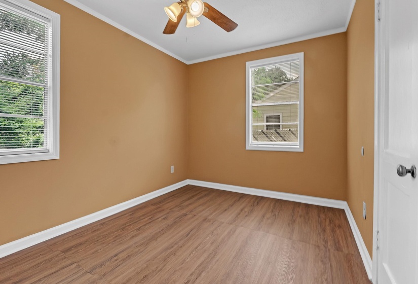 Spacious room featuring wood-finish flooring, two windows with blinds, a ceiling fan with light fixture, and a white interior door
