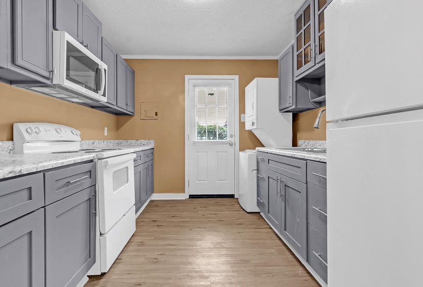 Galley kitchen featuring wood-finish flooring, grey cabinetry, light-toned countertops, and a white appliance package