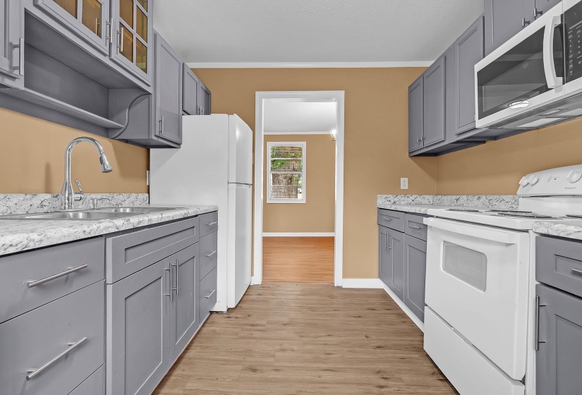 Kitchen featuring gray cabinetry, light countertops, wood-finish flooring, and white appliances including a refrigerator, range, and microwave