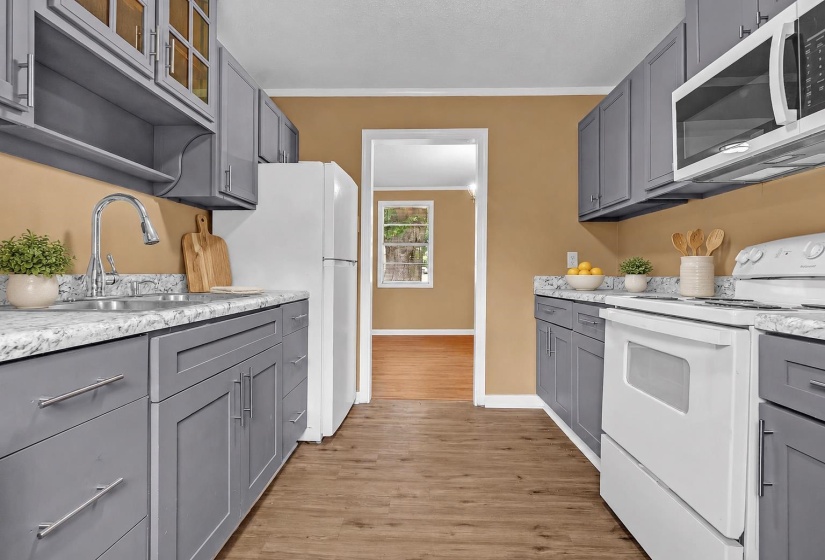 Galley kitchen featuring gray shaker-style cabinetry, white appliances, speckled countertops, and wood-finish flooring