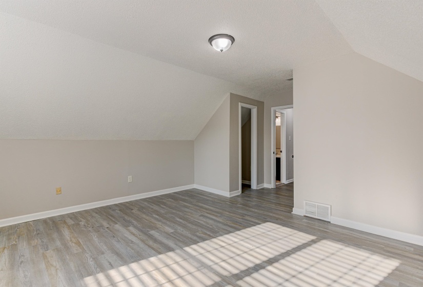 Additional living space with lofted ceiling, light wood-style flooring, and a textured ceiling