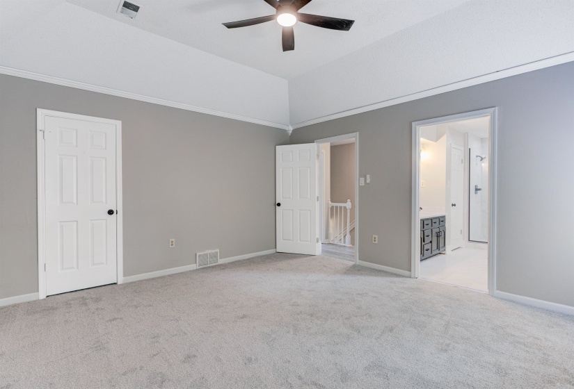 Unfurnished bedroom featuring light colored carpet, vaulted ceiling, a ceiling fan, and ensuite bath