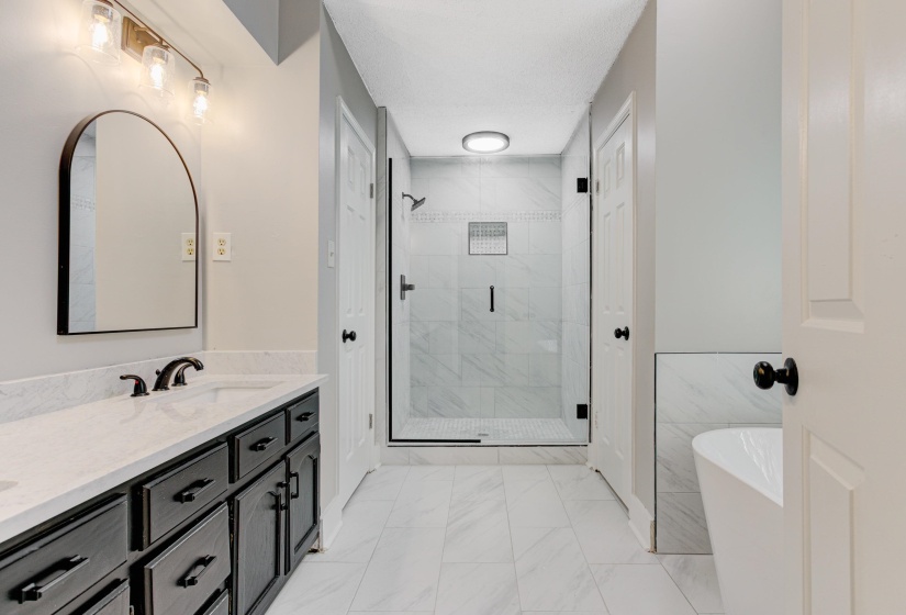 Bathroom featuring a stall shower, a freestanding tub, double vanity, and light marble finish floors
