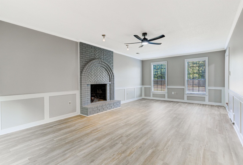 Unfurnished living room featuring a brick fireplace, light wood finished floors, a decorative wall, ornamental molding, and a ceiling fan