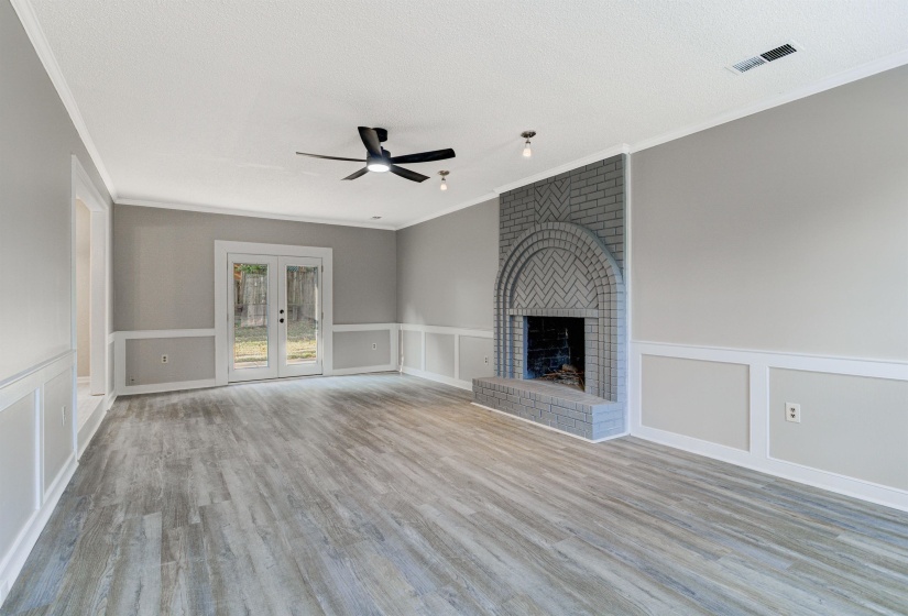 Unfurnished living room with a decorative wall, a fireplace, a wainscoted wall, light wood-type flooring, and crown molding