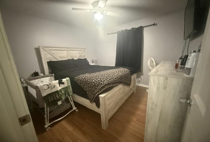 Wood-finish flooring with light gray walls, an overhead ceiling fan, and a window with dark privacy curtains