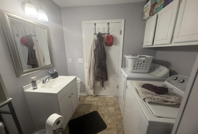 Compact laundry area featuring white upper cabinetry, a utility sink with white vanity, and a mirrored wall fixture with overhead lighting