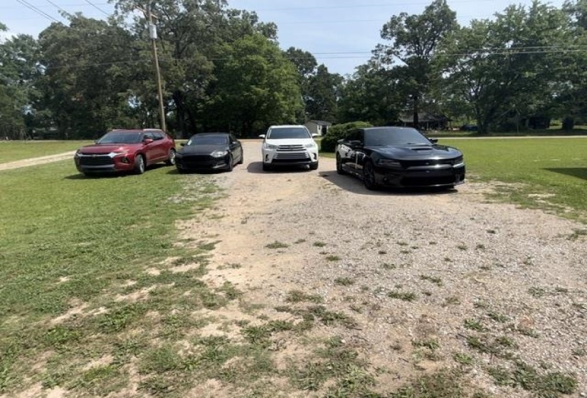 Gravel driveway offering ample parking space, bordered by a green lawn and mature trees