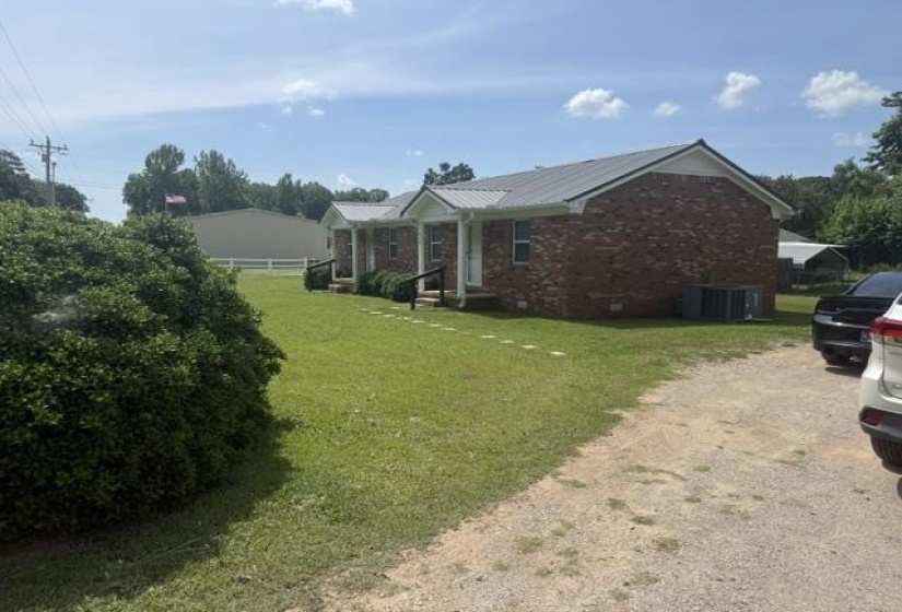Brick exterior featuring a metal roof, front entryways with black railings, and a gravel driveway